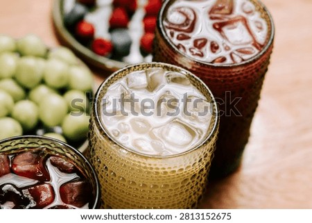 Refreshing iced drinks in patterned glass tumblers served with bowls of green grapes and berries on a wooden surface during the afternoon.