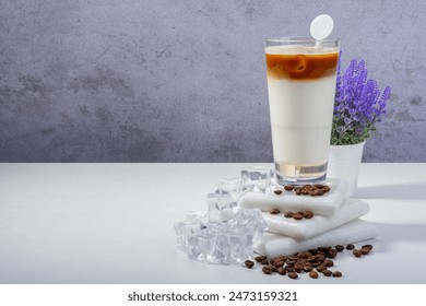 A refreshing iced latte scene with a glass of iced coffee and milk, ice cubes, coffee beans, and a potted lavender plant on a white table. Inviting and cool atmosphere. - Powered by Shutterstock