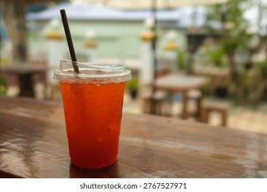Refreshing iced lemon tea in a plastic takeaway cup with a straw placed on a rustic wooden table at an outdoor cafe.