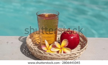 Refreshing iced tea with apple and flowers on a poolside surface