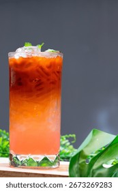 Refreshing iced Thai tea with gradient orange and pink layers, served in a tall glass with ice cubes and mint leaves.