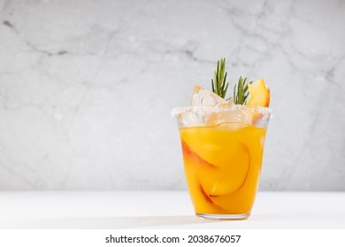 Refreshing Juicy Peach Cocktail With Ice, Rosemary, Sugar Rim, Fruit Slices In Misted Glass On White Wood Table, Concrete Wall.