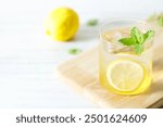 Refreshing lemonade drink with ice, sliced lemon and mint. Cold lemonade on white wooden table background.