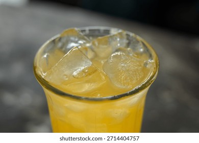 Refreshing macro close-up view of vibrant chilled citrus beverage with texture of melting ice cubes filling the clear glass.