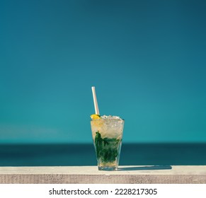A refreshing Mojito cocktail served on a wooden table. Shot on a hot summer day in Lozenets, Bulgaria in front of a clear sky over the open sea in the background.