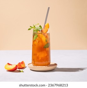 Refreshing peach ice and mint tea. Vegan homemade cold summer drink on tall glass on a light background with fresh fruits and shadows. Front view and free space for text.