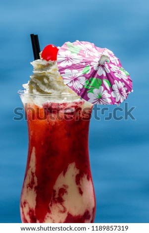refreshing pina colada served with blended berries as a garnish and topped with whipped cream with a natural blue water background as a travel holiday concept