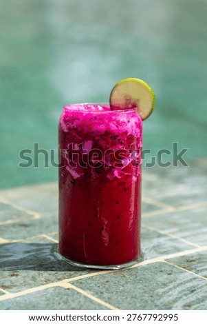 Refreshing pink dragon fruit smoothie with lime slice resting on poolside tiles