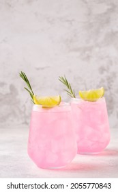 Refreshing Pink Drink Or Cocktail With Ice, Garnished With A Slice Of Lime And Rosemary.