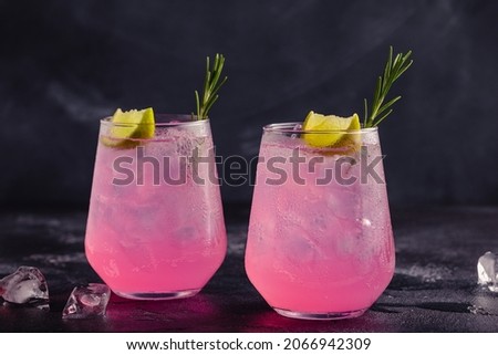 Refreshing pink drink or cocktail with ice, garnished with a slice of lime and rosemary.