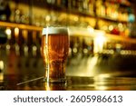 Refreshing pint of beer with bright foam and cold drops standing in front of bar taps and shelves. Concept of alcohol, festival, beer, culture, pub, bar, celebration, Friday mood.