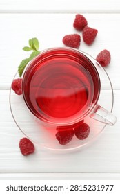 Refreshing raspberry tea in glass cup, fresh berries and mint leaves on white wooden table, flat lay