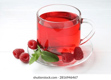 Refreshing raspberry tea in glass cup, fresh berries and mint leaves on white wooden table, closeup