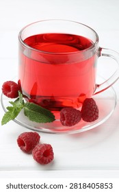 Refreshing raspberry tea in glass cup, fresh berries and mint leaves on white wooden table, closeup