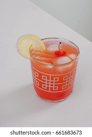 Refreshing Shirley Temple Cocktail On A White Table. Garnished With A Lemon And Cherries With A Stem. This Is A Classic Recipe For A Non-alcoholic Summer Drink.