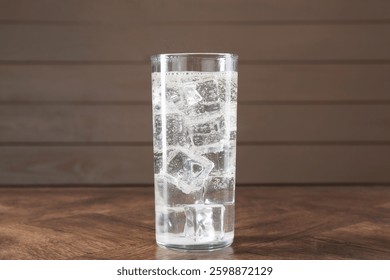 Refrescante agua de soda con cubitos de hielo en vidrio sobre mesa de madera