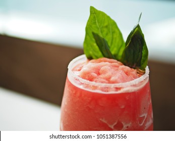Refreshing summer drink with a glass of watermelon rose frappe or smoothie decorated by sweet basil leaves in red wine glass on beautiful blurred background. Enjoy summer concept! (selective focus)