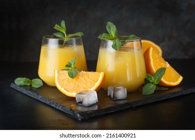 Refreshing summer drink with orange juice, mint and ice cubes in glasses on a wooden table