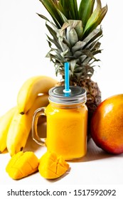 Refreshing Summer Mango Ananas Banana Smoothie: Low Calories Drink. Sweet Fruity Dessert For Summer Beach Party.  In A Jar With Blue Straw. Slices Of Mango As Decor. White Background