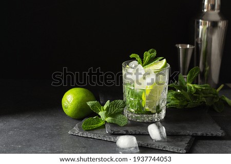Refreshing summer mojito cocktail with ice cubes, fresh mint and lime on black. Exotic mojito beverage.