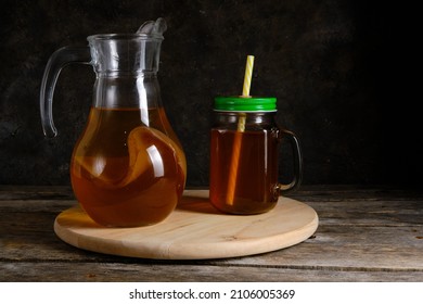 Refreshing summer mushroom tea drink in jug and mug with straw is illuminated by daylight on dark background - Shutterstock ID 2106005369