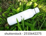 Refreshing water in white thermo stainless bottle on the grass.