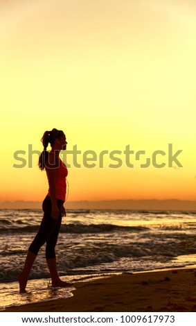 Refreshing wild sea side workout. Silhouette. Full length portrait of healthy woman in sportswear on the beach walking