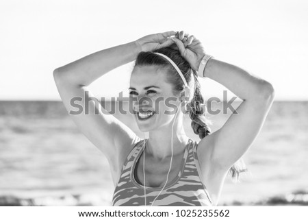 Refreshing wild sea side workout. smiling healthy woman in sport clothes on the seashore looking into the distance and listening to the music with headphones