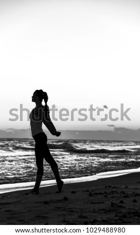 Refreshing wild sea side workout. Silhouette. Full length portrait of healthy woman in sportswear on the seacoast stretching
