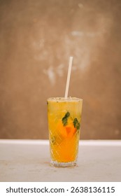 Refreshing yellow drink with mint and orange served in a tall glass on a simple background