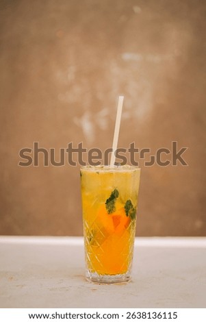 Refreshing yellow drink with mint and orange served in a tall glass on a simple background