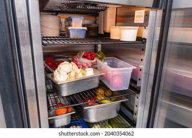 Refrigerator of restaurant with food. Vegetables in restaurant refrigerator. Containers with vegetables on shelves of refrigerator. Radishes, cauliflower and pears in fridge camere.