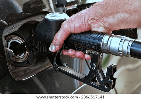 Refueling the car, a man's hand refills diesel fuel at the gas station and the gasoline pump fills the fuel nozzle in the car tank.