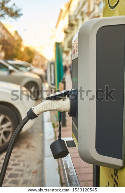 refueling an electric car at a charging\
station.  Cars are visible in the\
background.