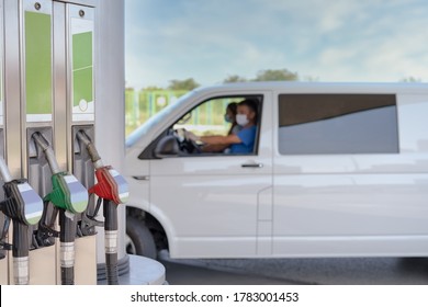 Refueling Hoses At A Gas Station With A Van In The Background And People Wearing Masks