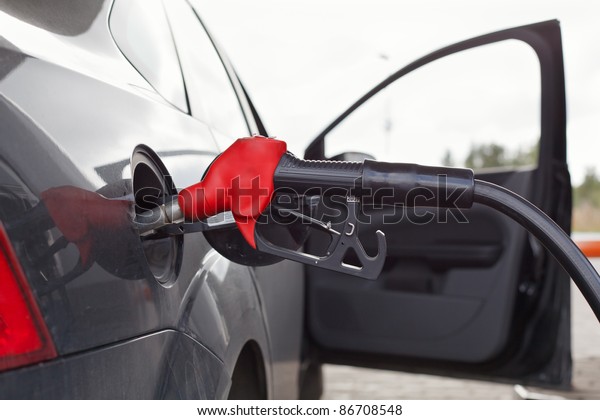 Refueling nozzle in the tank car at a fuel filling\
column. Summer day. Black\
car