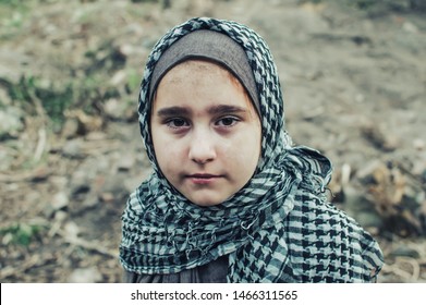 a refugee child in the war, a Muslim girl with a dirty face on the ruins, the concept of peace and war, the child is crying and waiting for help.