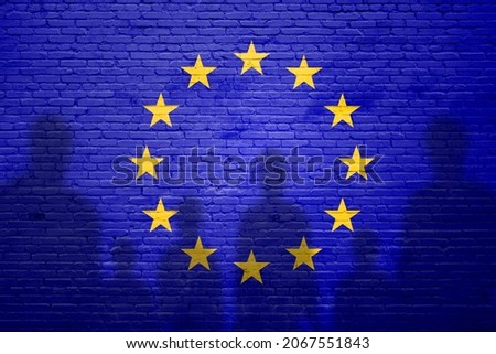 The refugees migrate to Europe union . Silhouette of immigrants . Europe union migration policy. Europe Union flag painted on a brick wall