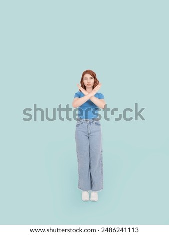 Refusing concept image, full body view young caucasian 20s woman standing over light blue background showing stop gesture with crossed hands. Serious girl, refusing unwanted something. Copy space.