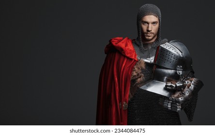 Regal portrait of a young king in armor with steel plates, holding a steel helmet and wearing a red cloak, posing on a neutral background