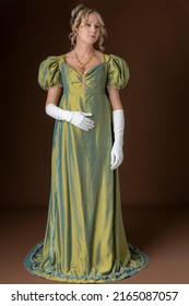 A Regency Woman Wearing A Green Shot Silk Gown And White Gloves And Standing Against A Studio Backdrop