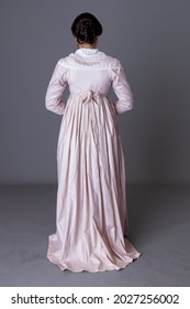 A Regency Woman Wearing A Pink Cotton Dress Against A Grey Studio Backdrop