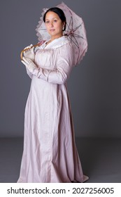 A Regency Woman Wearing A Pink Cotton Dress Against A Grey Studio Backdrop