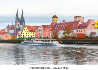 Regensburg city on a river in Bavaria , Germany . Tourist boat on the Danube river in Regensburg . Clock tower and cathedral at riverside in autumn 