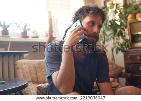 Reggae hippie man sitting in his living room, having a chat on his cell phone, sitting in a nice salon and a stylish armchair