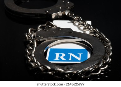 Registered Nurse Badge Surrounded By Steel Handcuffs On A Black Background Indicating A Medication Error Or Med Error