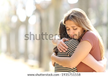 Regretful woman embracing a friend reconciliating in the street