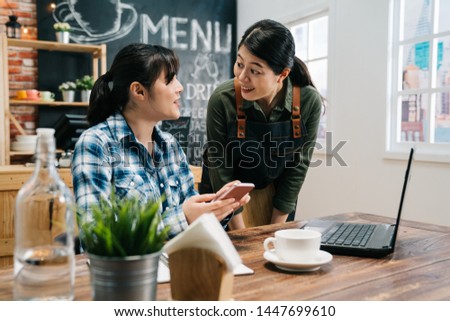 Regular customer concept. Cheerful nice woman cafe bar worker look friend smiling chatting with funny news on social media. female barista in apron standing by loyal visitor freelance in coffee shop
