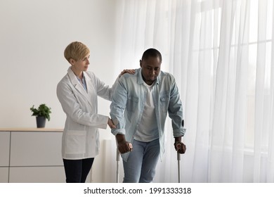 Rehab clinic, recovery support and assistance of medical professional. Serious adult woman doctor teach stressed mature african american man to walk with crutches in living room or clinic interior - Powered by Shutterstock