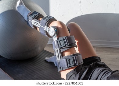 Rehabilitation after knee surgery. Woman wearing sport clothes and orthosis doing exercises using fitness ball - Powered by Shutterstock